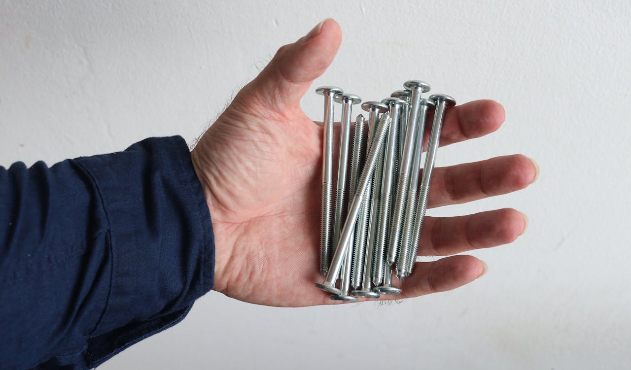 A hand holds several metal screws against a white background.